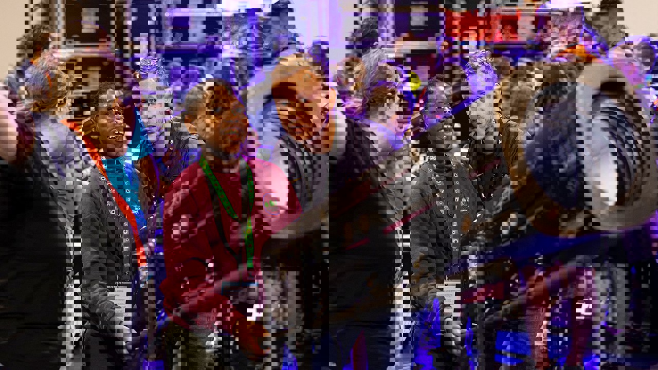 A young person smiling at The Big Bang Fair. Adults are showing them how to operate a theatre light