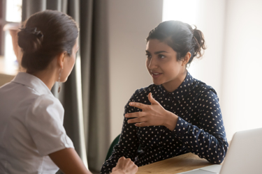 Two people in discussion, facing each other. One has their back turned to the camera. 