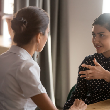 Two people in discussion, facing each other. One has their back turned to the camera. 