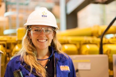 A female apprentice in a hard hat looking at the camera
