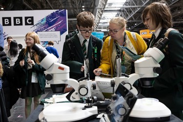 Several young people and a teacher at a scientific display study and interact with the equipment, they are at The Big Bang Fair