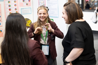 A young person at their Big Bang Competition stand at The Big Bang Fair shows their Competition entry to two visitors