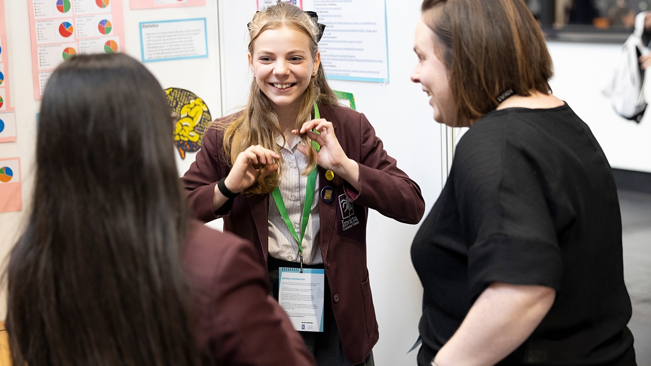 A young person at their Big Bang Competition stand at The Big Bang Fair shows their Competition entry to two visitors