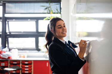 Secondary school student in a classroom writing on a whiteboard.