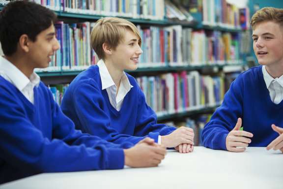 Three young people in a school library sit at a table having an animated discussion