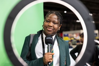 A young person at The Big Bang Fair holds a microphone ad looks through a ring lamp directly into camera