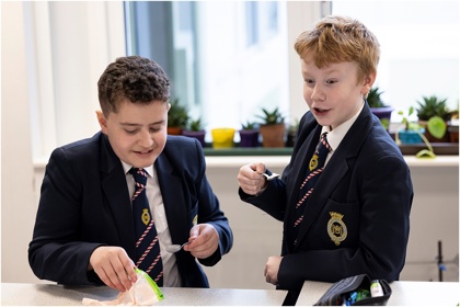 Two young people in a school science lab work on an experiment. They smile. 