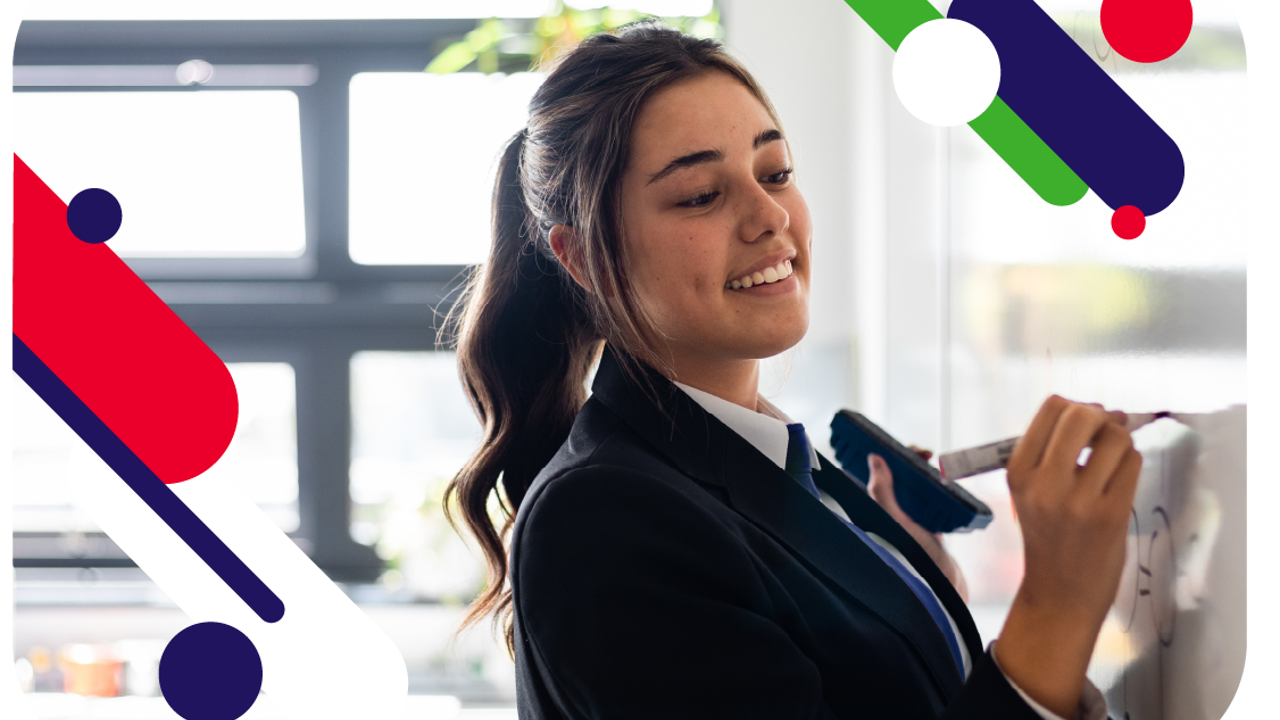 Young person writing on a whiteboard and smiling. They are wearing school uniform. 