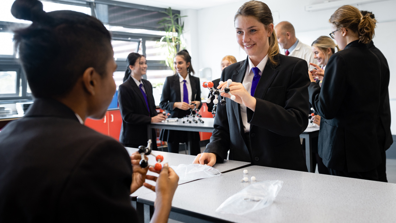 Several secondary school pupils and a teacher in a classroom partaking in a science lesson. Some students are doing experiments while others watch.