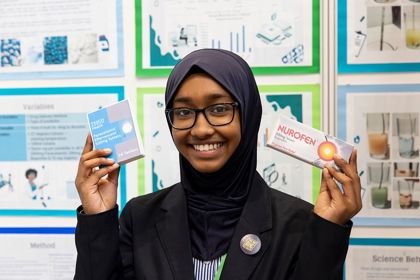 The Big Bang Competition's UK Young Scientist of the Year winner stands and smiles at the camera surrounded by her working boards and sketches that show how her winning idea developed