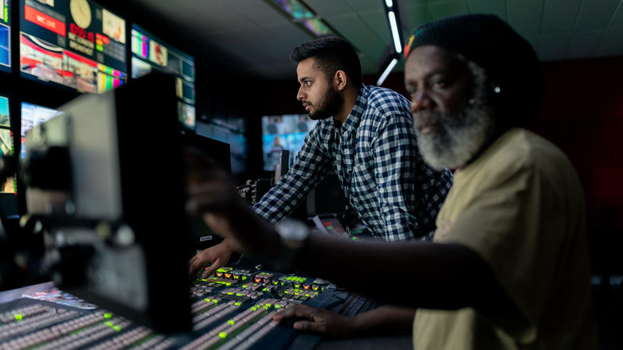 Two sound engineers in a broadcast studio checking equipment and levels