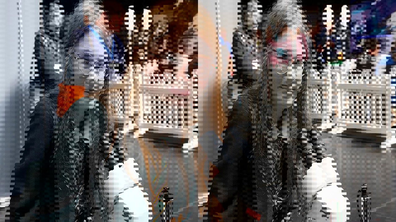 A young person at The Big Bang Fair stands in front of a microscope and looks into camera 