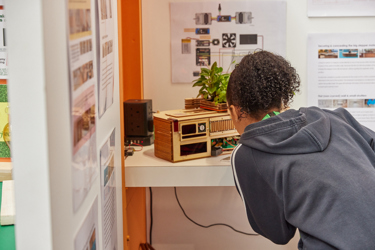 A booth featuring display boards to explain how a scientific competition entry evolved. A young person with their back to the camera bends down and peers at the scale model on display.