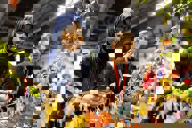 A young person at The Big Bang Fair interacts with coloured leaves at the Tree Council stand as they smile at the camera