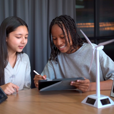 Two young people study a screen. A wind turbine is on the table between them. 