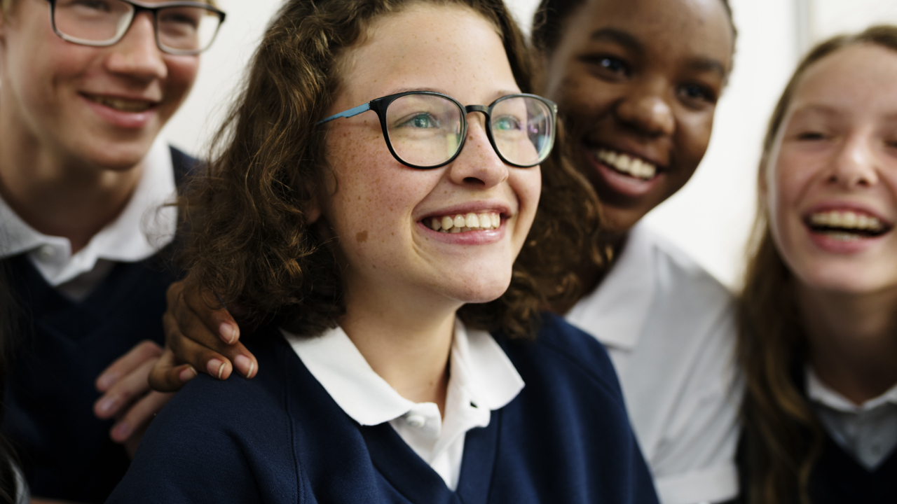 Four school students stand close together as they smile 