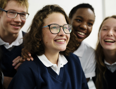 Four school students stand close together as they smile 