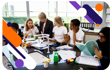 A group of young people in a school science lab working as they sit around a bench. A teacher stands and chats to them.