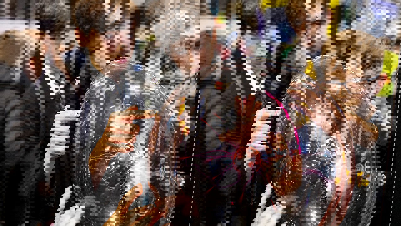 Six hands touch a plasma ball on display at The Big Bang Fair. Four young people are watching the effects.