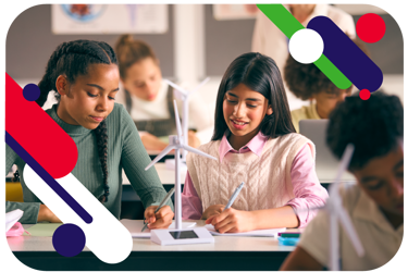Young people in a classroom setting, sitting at their desks. There are small models of wind turbines on their desks as they work with their models and notebooks.