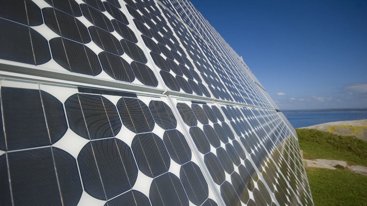 A close up of a large solar panel. In the distance there is landscape and blue sky.