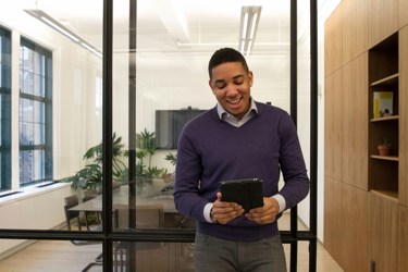 An adult stands in front of an empty boardroom with an iPad, looking animated