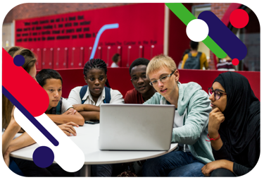 Young people in a school setting, sitting around a desk. They are all looking at a laptop screen. 