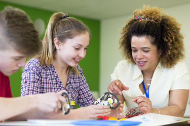 Teacher helping two secondary school students build a robotic arm in their design and technology lesson