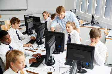 Seven students and a teacher work in a school computer lab. All the young people are looking at their individual screens on their desks.