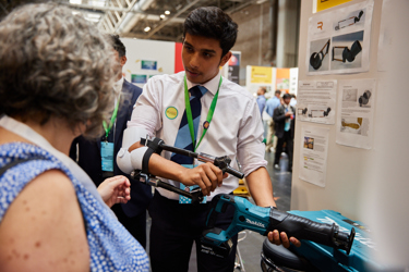 A Big Bang Competition entrant shows their entry to a visitor to their stand at The Big Bang Fair. They are holding an implement to demonstrate how their idea works.