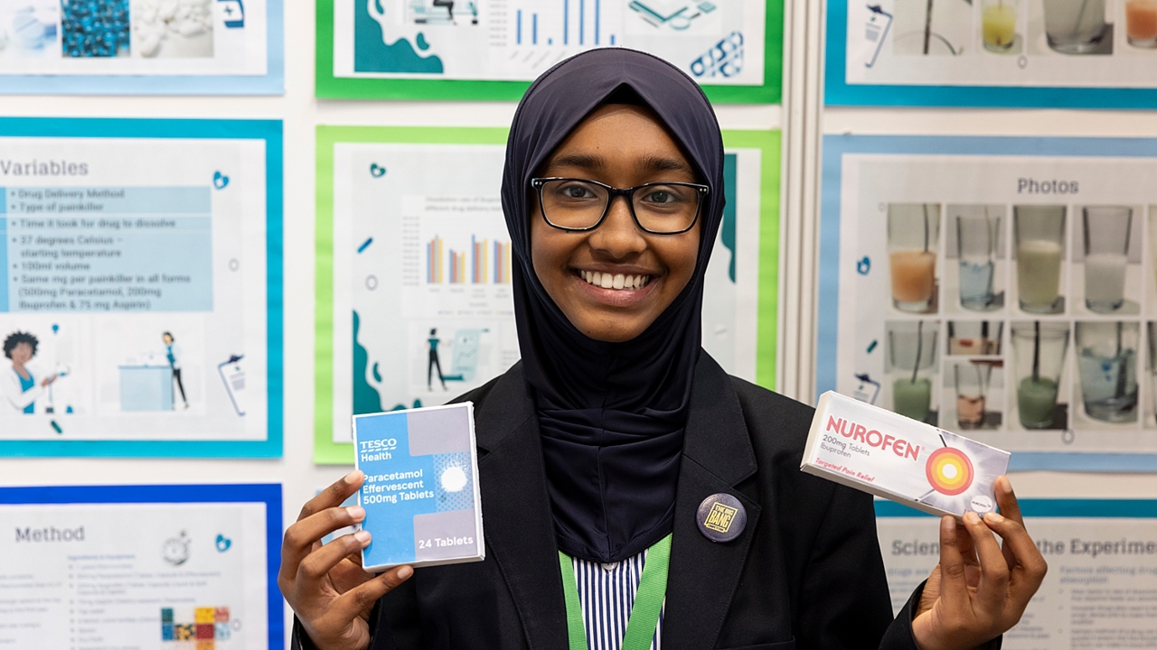 The Big Bang Competition's UK Young Scientist of the Year winner stands and smiles at the camera surrounded by her working boards, photographs and sketches that show how her winning idea developed