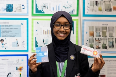 The Big Bang Competition's UK Young Scientist of the Year winner stands and smiles at the camera surrounded by her working boards, photographs and sketches that show how her winning idea developed