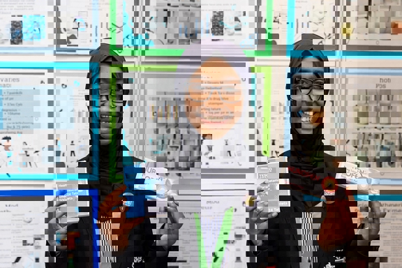 The Big Bang Competition's UK Young Scientist of the Year winner stands and smiles at the camera surrounded by her working boards, photographs and sketches that show how her winning idea developed